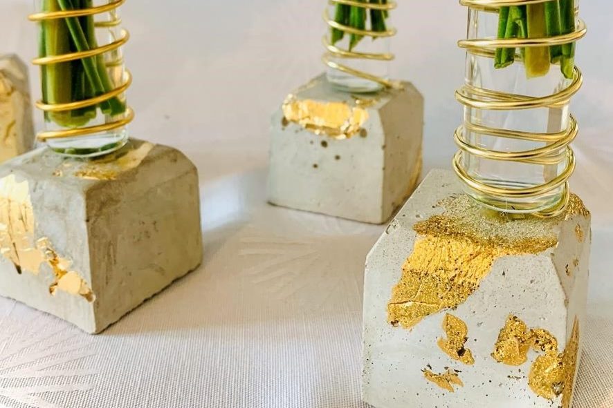 Betonvasen mit goldenen Akzenten und grünen Pflanzenstängeln.